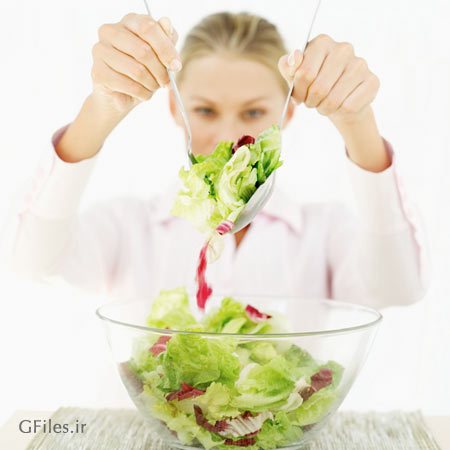 عکس ظرف شیشه ای سالاد که خانمی با قاشق و چنگال در حال سرو آن است